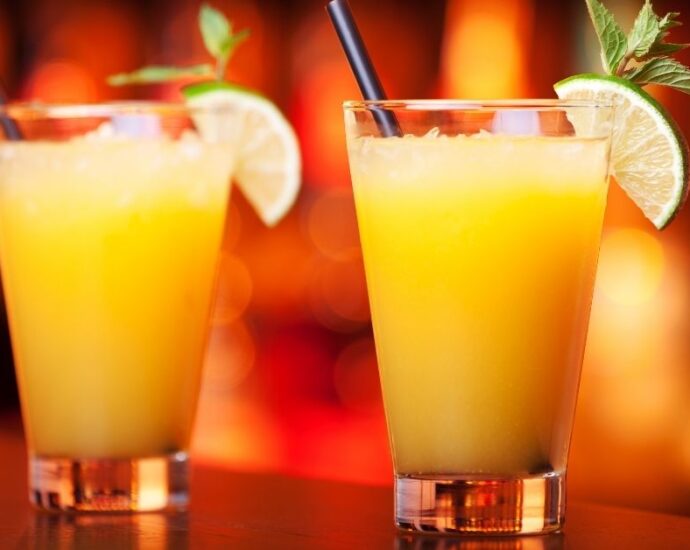 two glasses of a harvey wallbanger with a red orange background